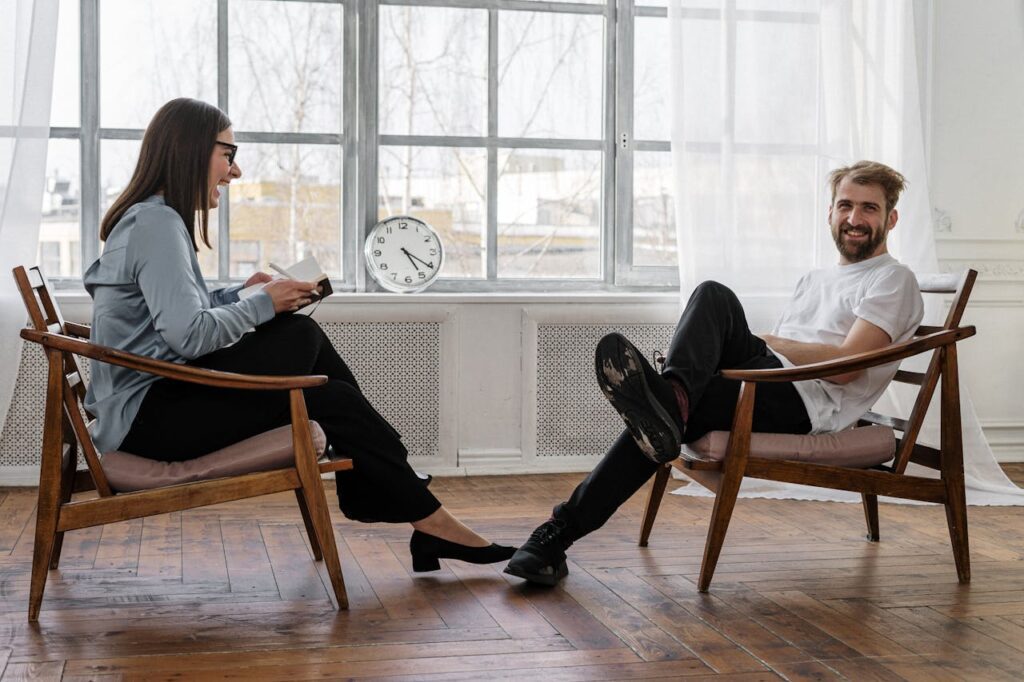 a man and a woman sitting opposite each other in chairs smiling and laughing. Possibly a coach situation. This is to represent good branding for coaches