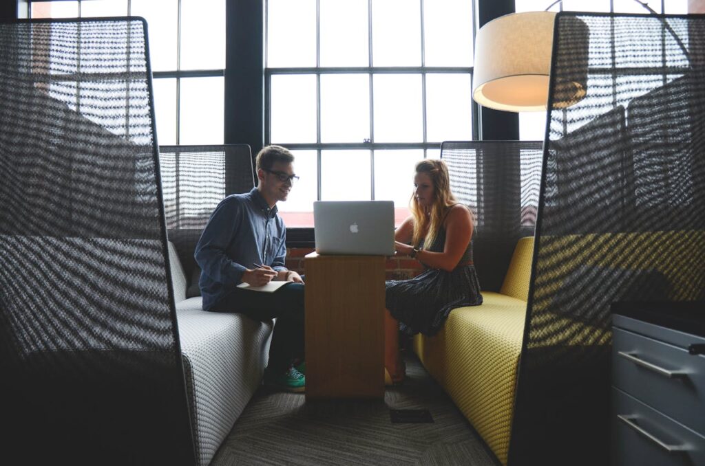 a man and woman looking at a laptop together. The man has a pen and paper as though he is taking notes.