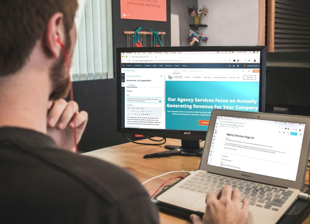why web design is important. It needs to reflect the company brand. A picture of a man on a laptop with a website open on a screen behind his laptop. He has earphones in.