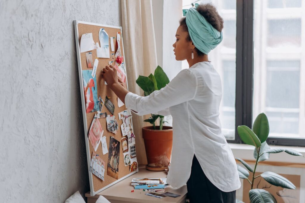 build your own brand identity by creating a moodboard. Its a picture of a woman pinning images into a cork board creating a mood board. She has a head scarf on and is of ethnic decent.