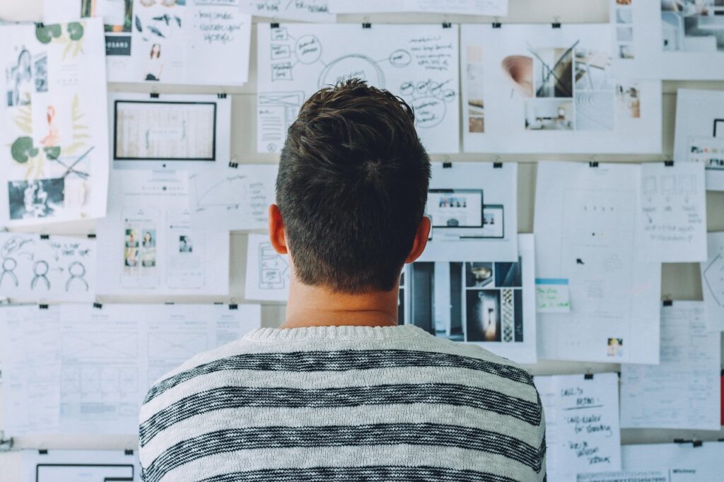 what is brand design? A picture of a man looking at a wall full of drawings and print offs that look like design based items.