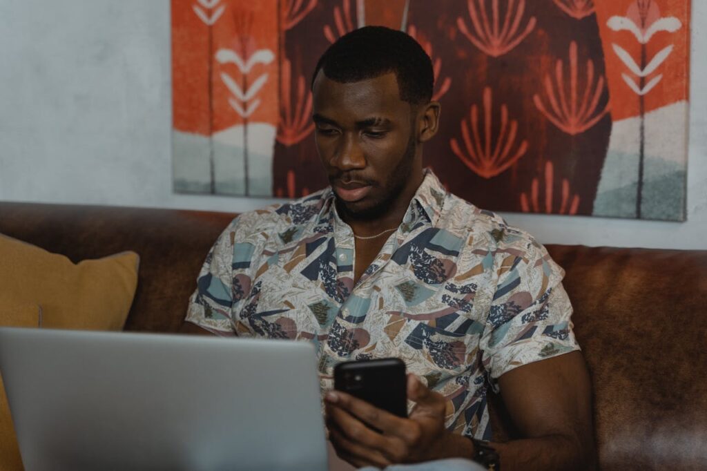 web design courses near me. A black man sitting on a sofa with a laptop on his knee.