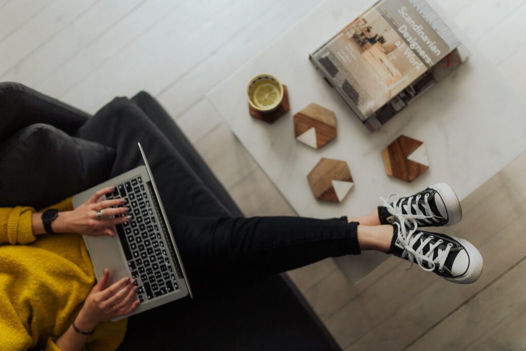 free stock photo websites - this is a picture from Kaboom Pics. A woman sitting on a laptop with a book about scandinavian designers at work on a table. Its a picture from a birds eye perspective. 