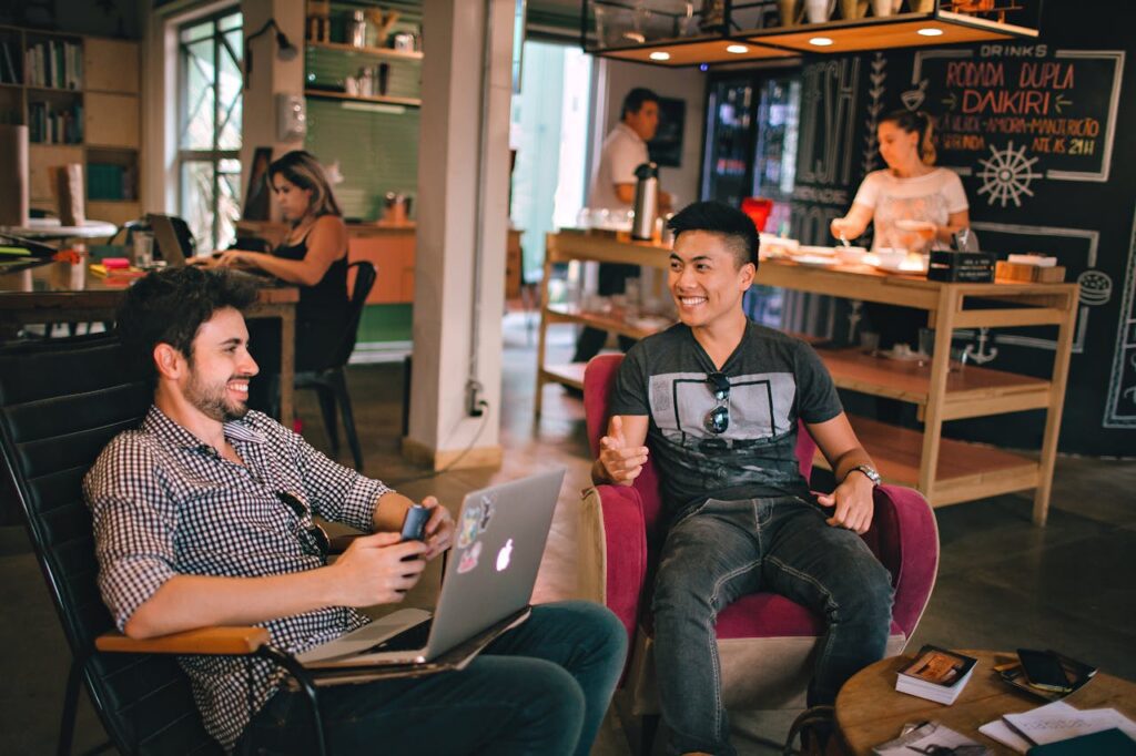 how to become a web designer from scratch. 2 men sitting in a coffee shop on a laptop smiling. This is to represent building web design projects for pretend coffee shops.