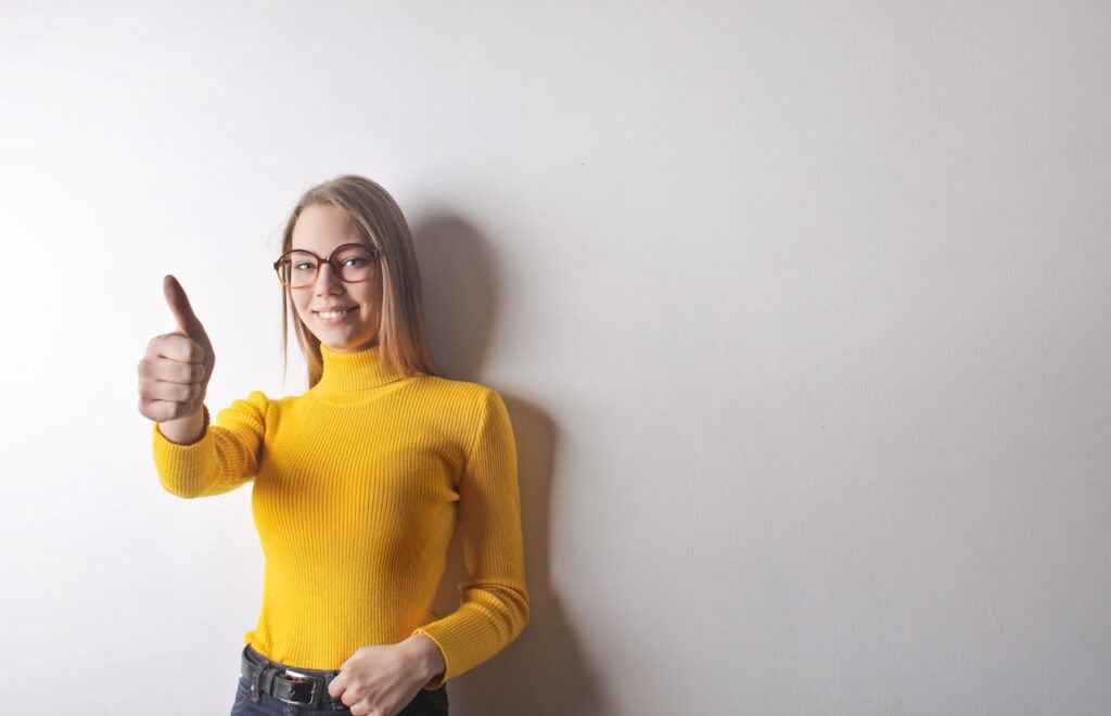 a branding coach can give you confidence. this woman in a yellow top gives a thumbs up and a smile. She is wearing glasses.
